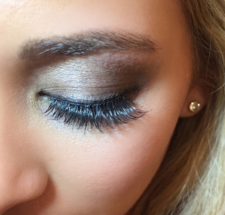 Close-up of a woman's eye with eye makeup and long eyelashes, wearing a small earring.
