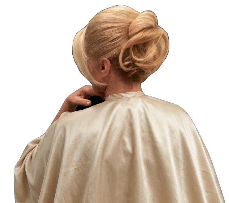 Back view of a woman with platinum blonde hair styled in an elegant updo, wearing a cream-colored satin cape or gown.