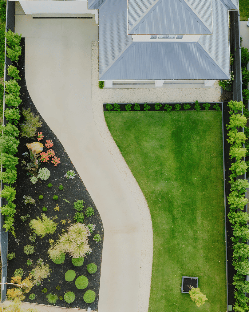 Aerial view of a backyard with a house, lawn, pathway, and garden with trees and plants.