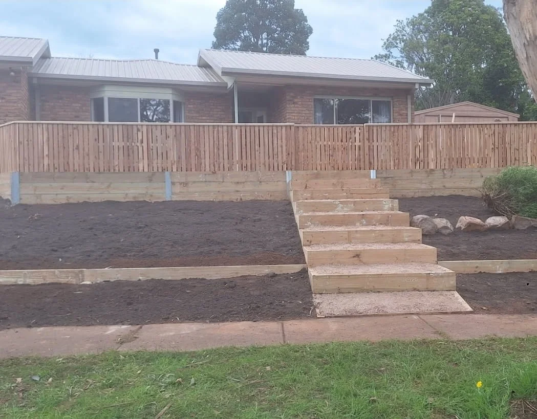 New wooden staircase leading up to a backyard patio with a wooden fence in front of a brick house.