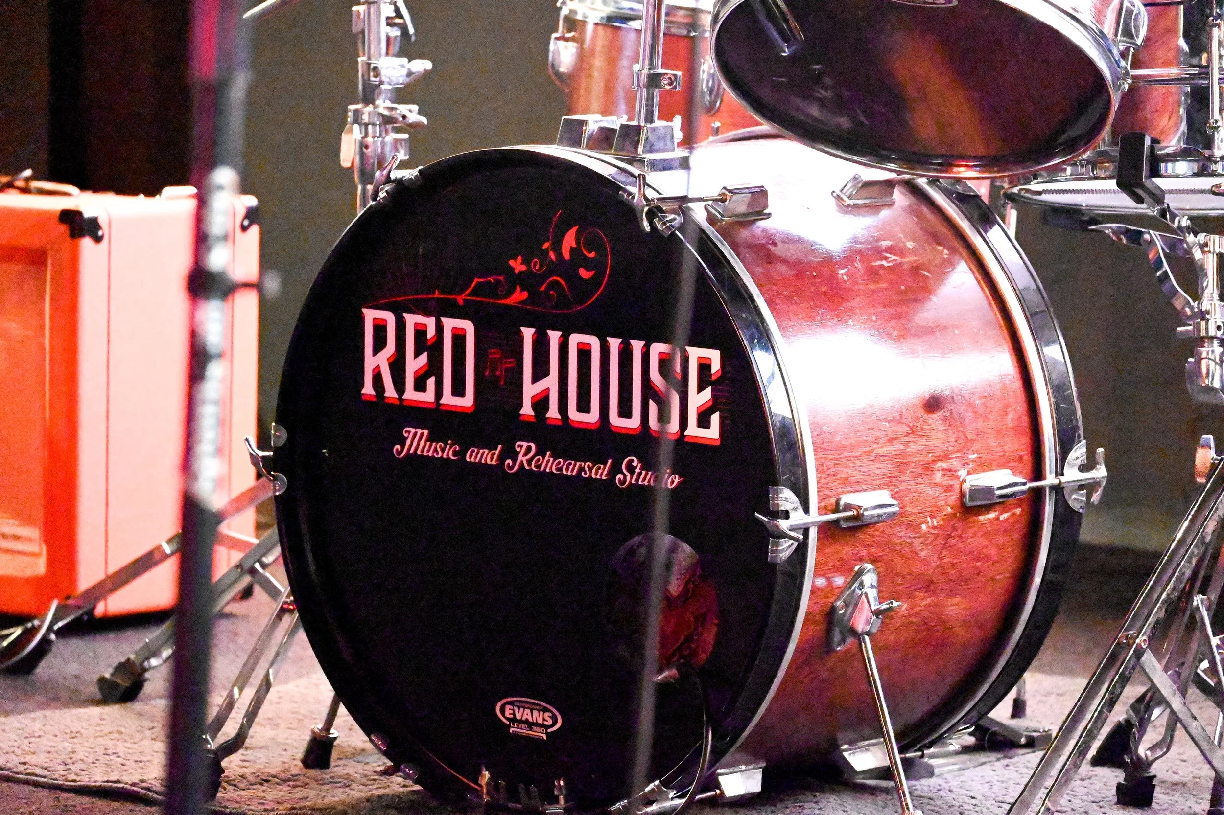 Electric guitar amplifier, drum kit with bass drum labeled "Red House Music and Rehearsal Studio," on stage with various musical equipment.