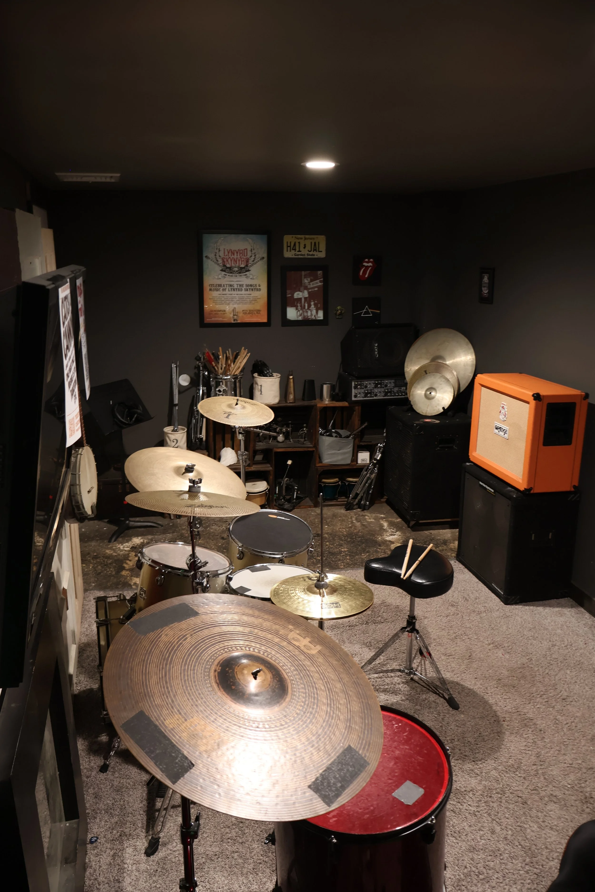 Music room with drums, cymbals, and musical equipment. Posters on the wall, including Lynyrd Skynyrd, and various music paraphernalia and amplifiers.