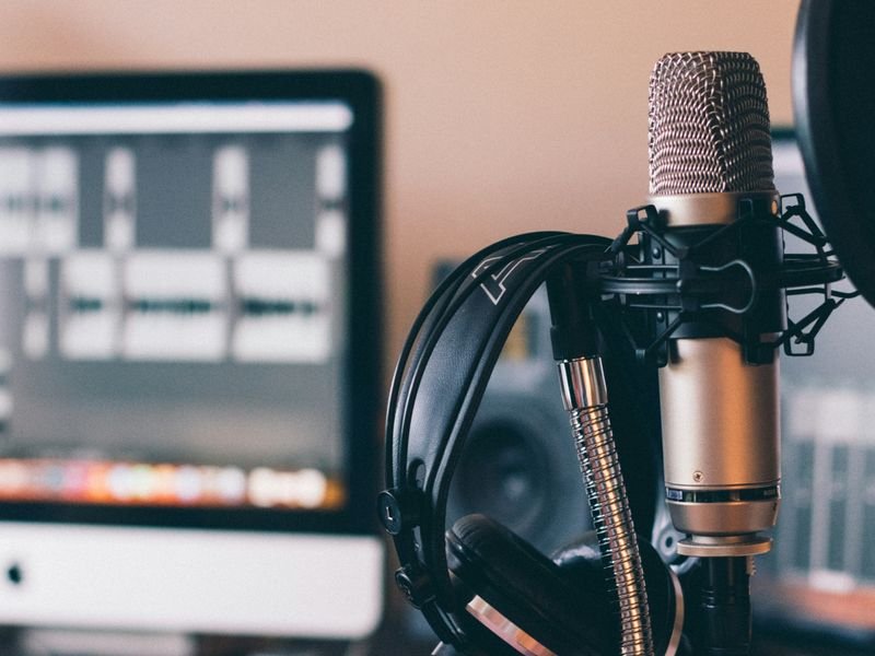 A professional recording setup with a large microphone, headphones hanging on the microphone stand, and a computer screen displaying audio editing software.