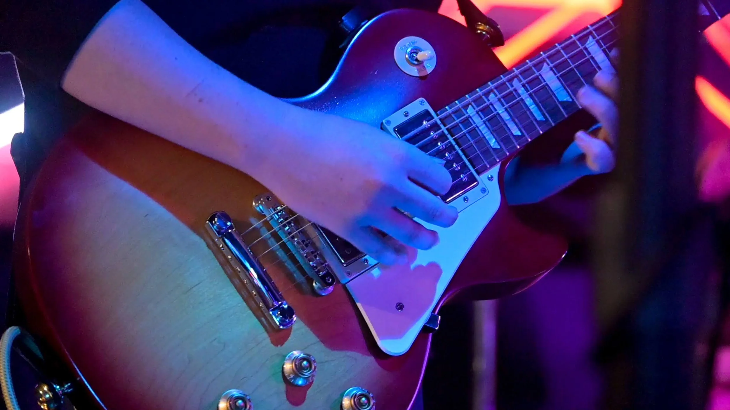 Close-up of a student playing an electric guitar under colorful stage lighting at a Red House Music and Rehearsal Studio performance.