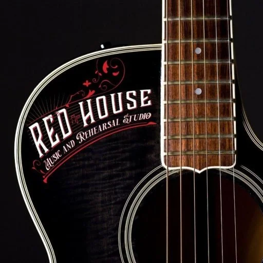 Close-up of an acoustic guitar with a black finish and the logo 'Red House Music and Rehearsal Studio' on the body