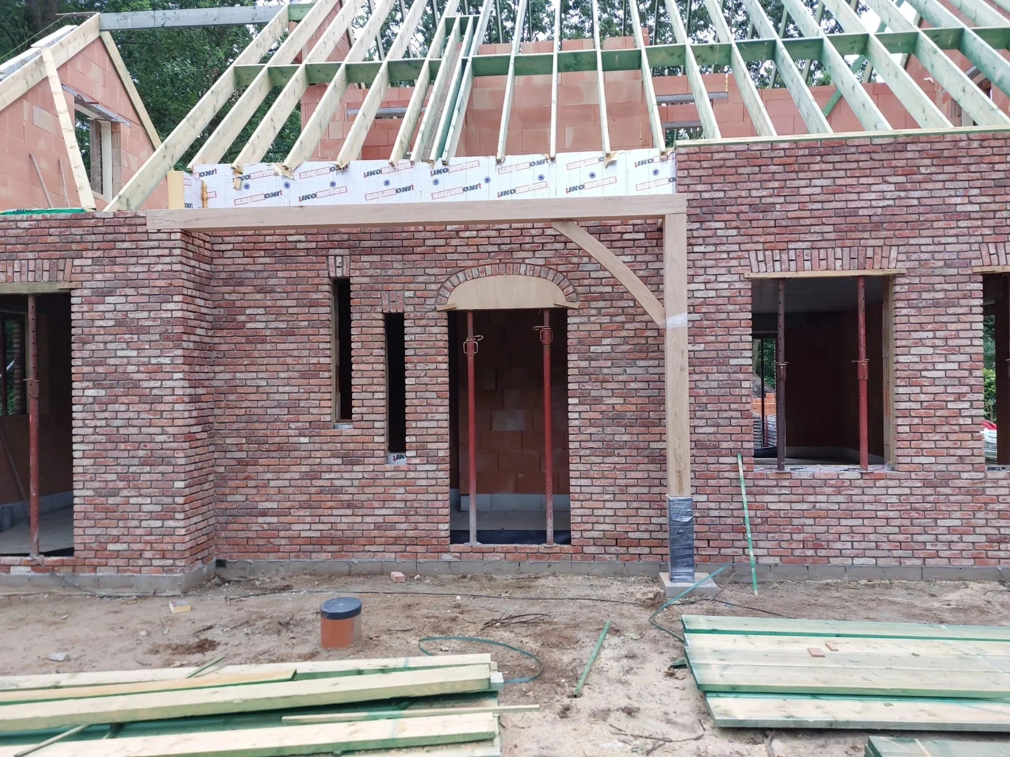 Een gebouw dat in aanbouw is, met een bakstenen muur en houten balken voor het dak.