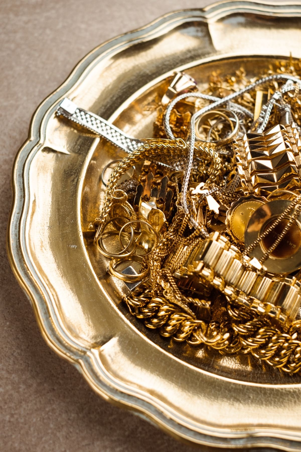 A gold decorative tray filled with assorted gold and silver jewelry, including chains, rings, and bracelets.