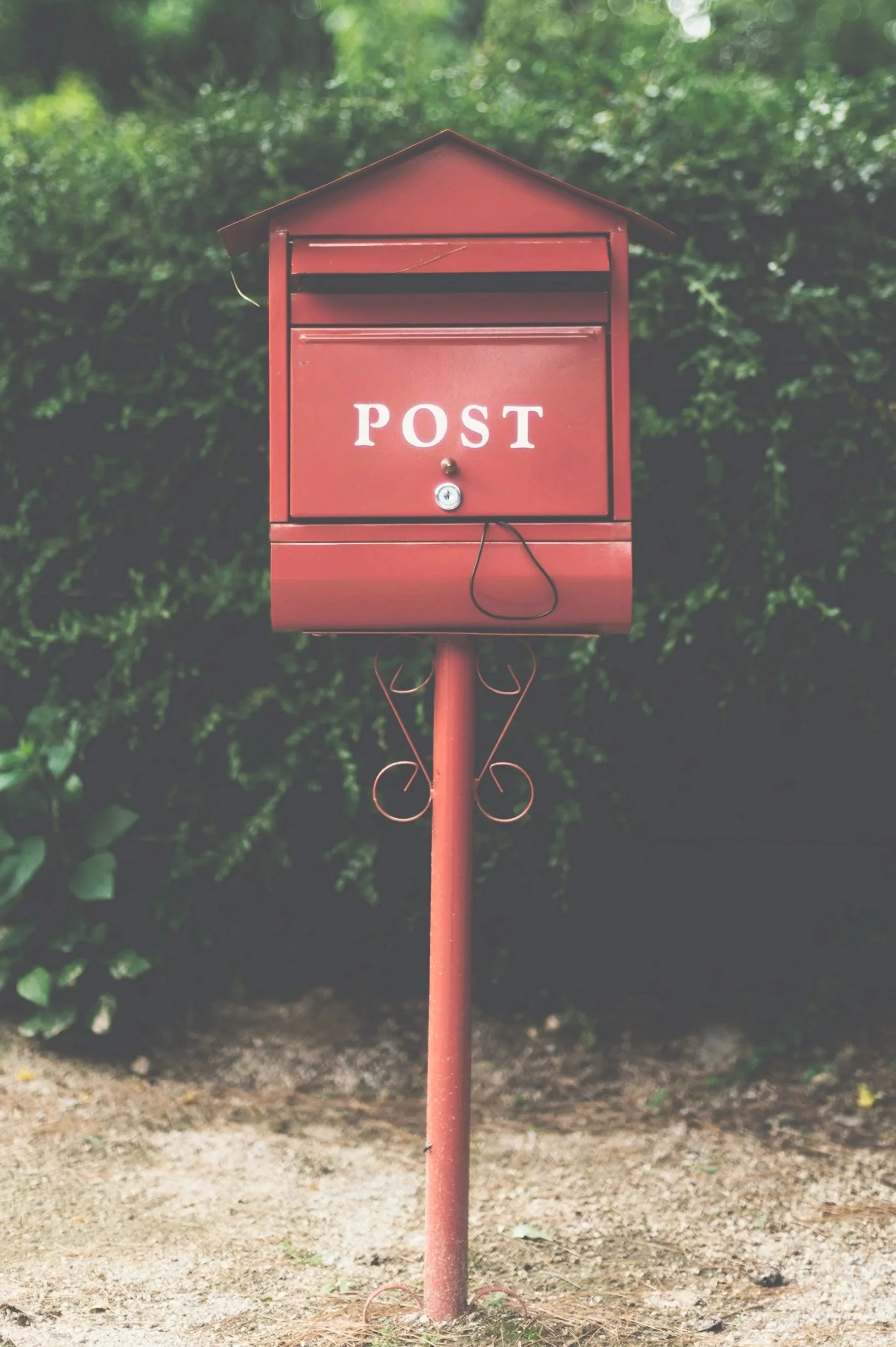 Red postbox in front of greenery