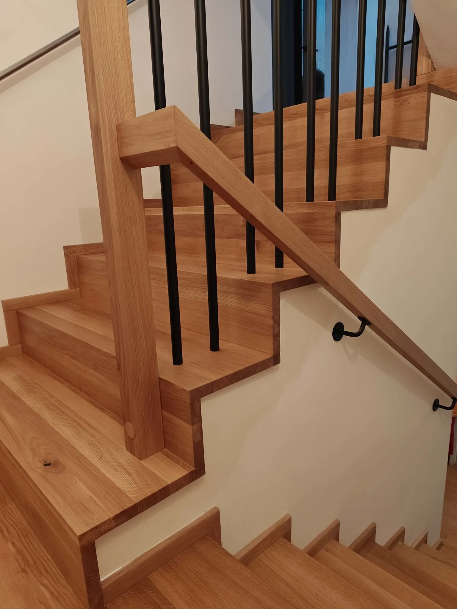 Wooden staircase with black metal railing and a beige wall.