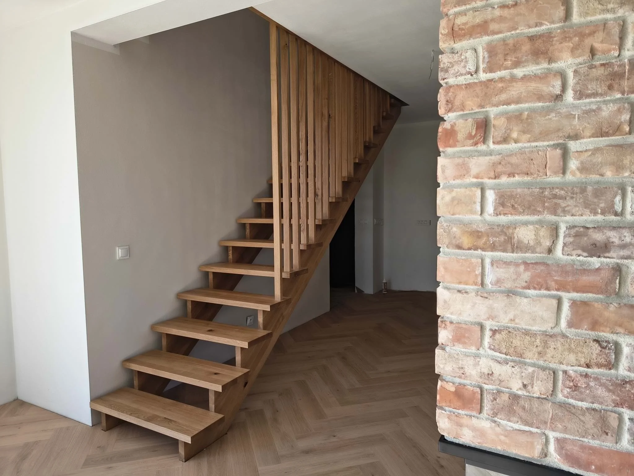 Wooden staircase with open risers next to a brick wall inside a home.