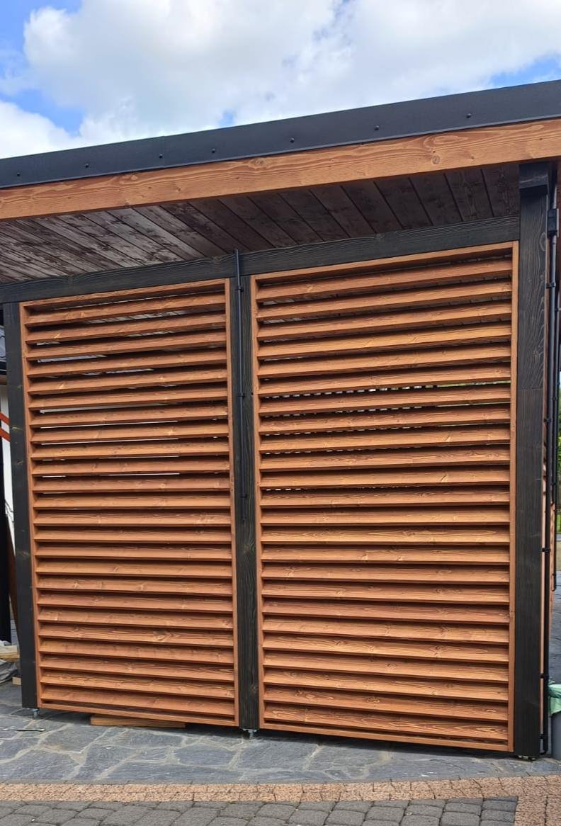 A modern wooden louvered sliding door with black metal framing outside a building with a stone walkway.