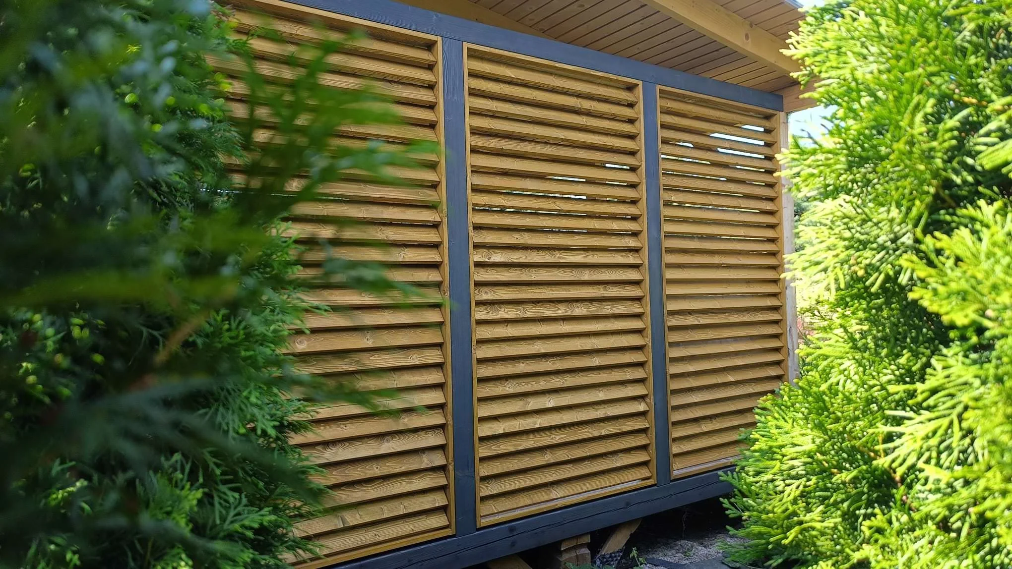 Wooden slatted privacy screen or fence with greenery on both sides.
