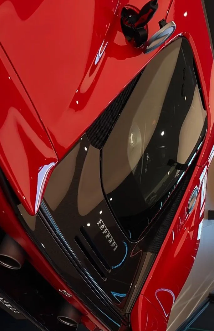 Close-up of a red Ferrari sports car showing the rear window, exhaust pipes, and part of the engine compartment with visible venting and branding.