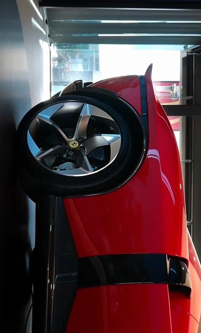 Red sports car with a large rear wing, viewed from the side, inside a showroom or garage.