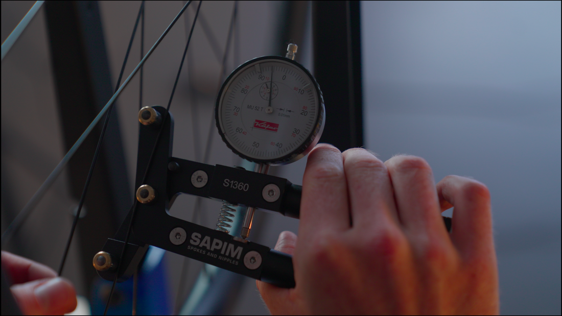 Close-up of a bicycle wheel being tensioned with a SAPIIM spoke tension meter.