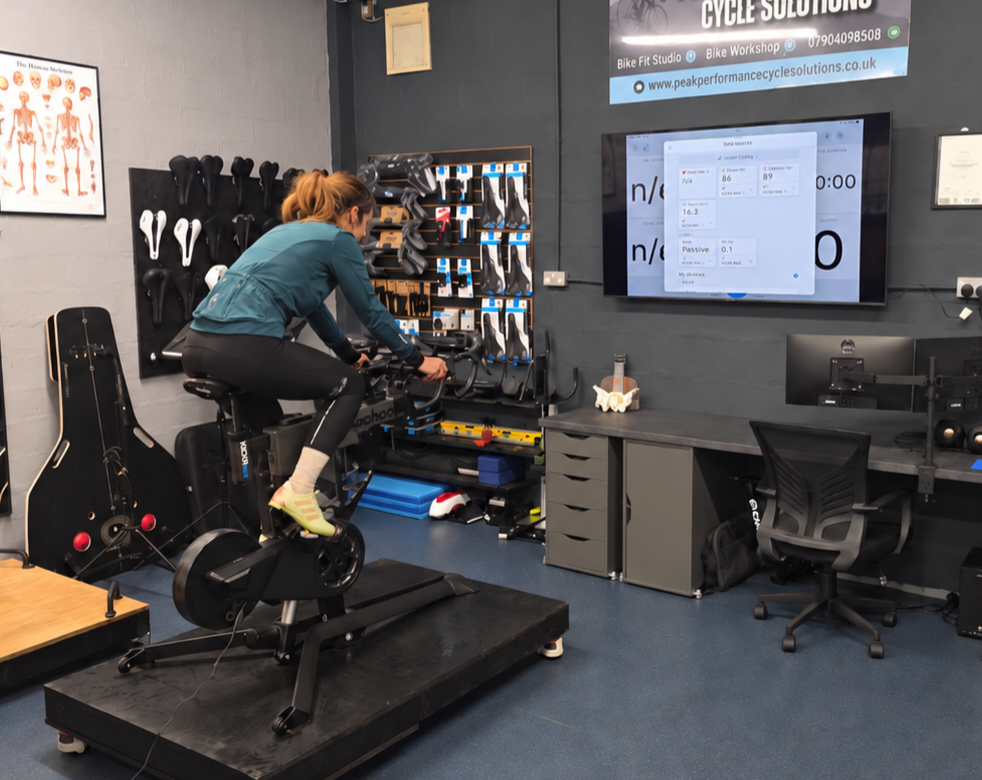 Cyclist undergoing an indoor bike fitting assessment on a stationary bike in a professional cycle workshop