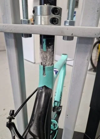 Close-up of a turquoise bicycle frame secured in a repair stand with the seatpost clamped.