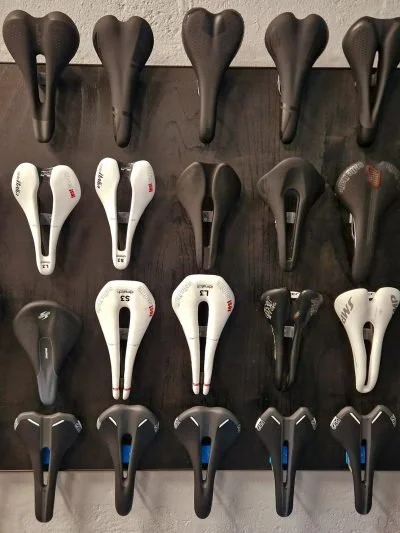 Display of assorted bicycle saddles arranged in rows on a dark wooden wall.