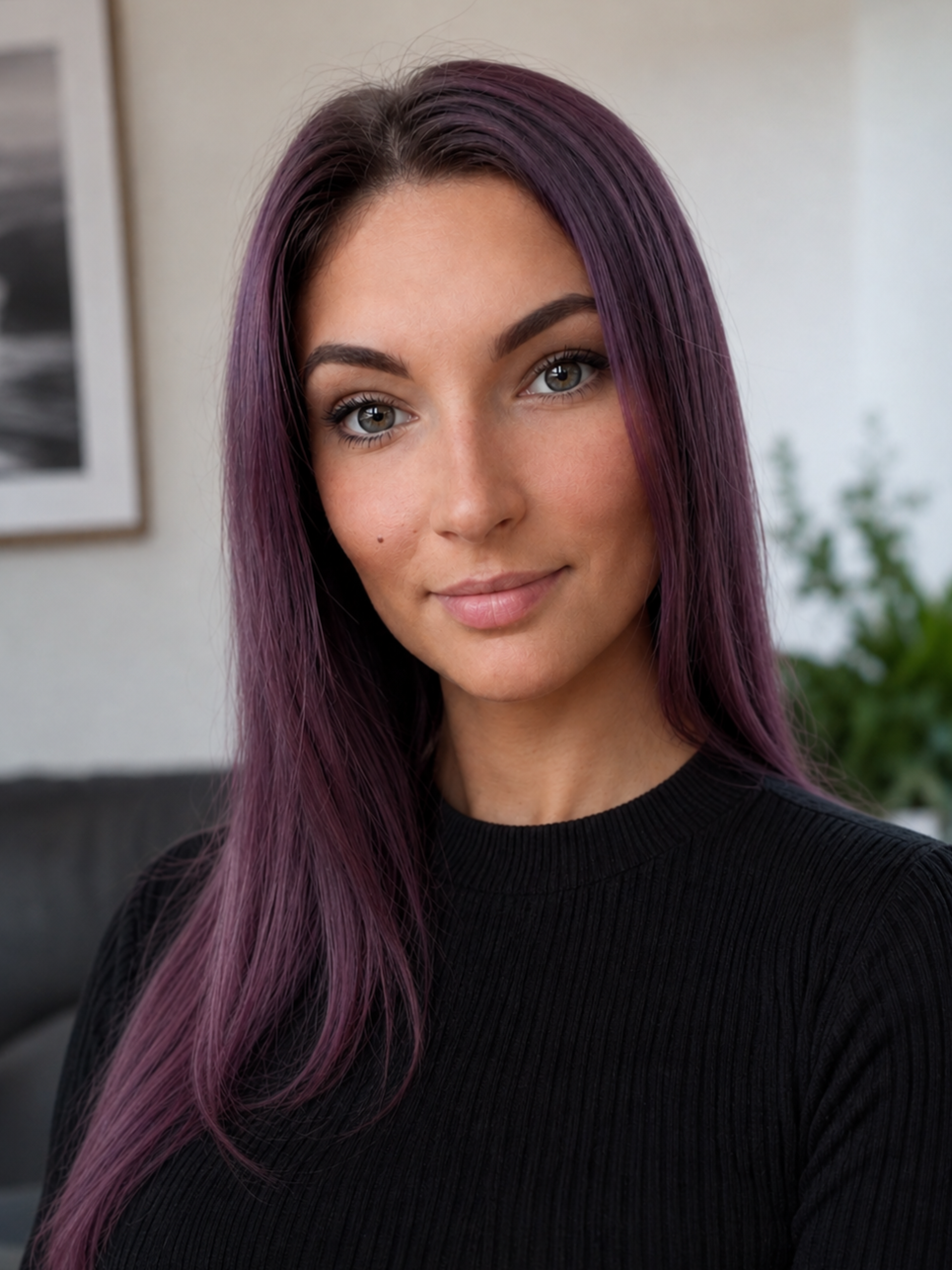 Portrait of a young woman with long purple hair, wearing a black ribbed shirt, smiling softly, indoors with a blurred background.