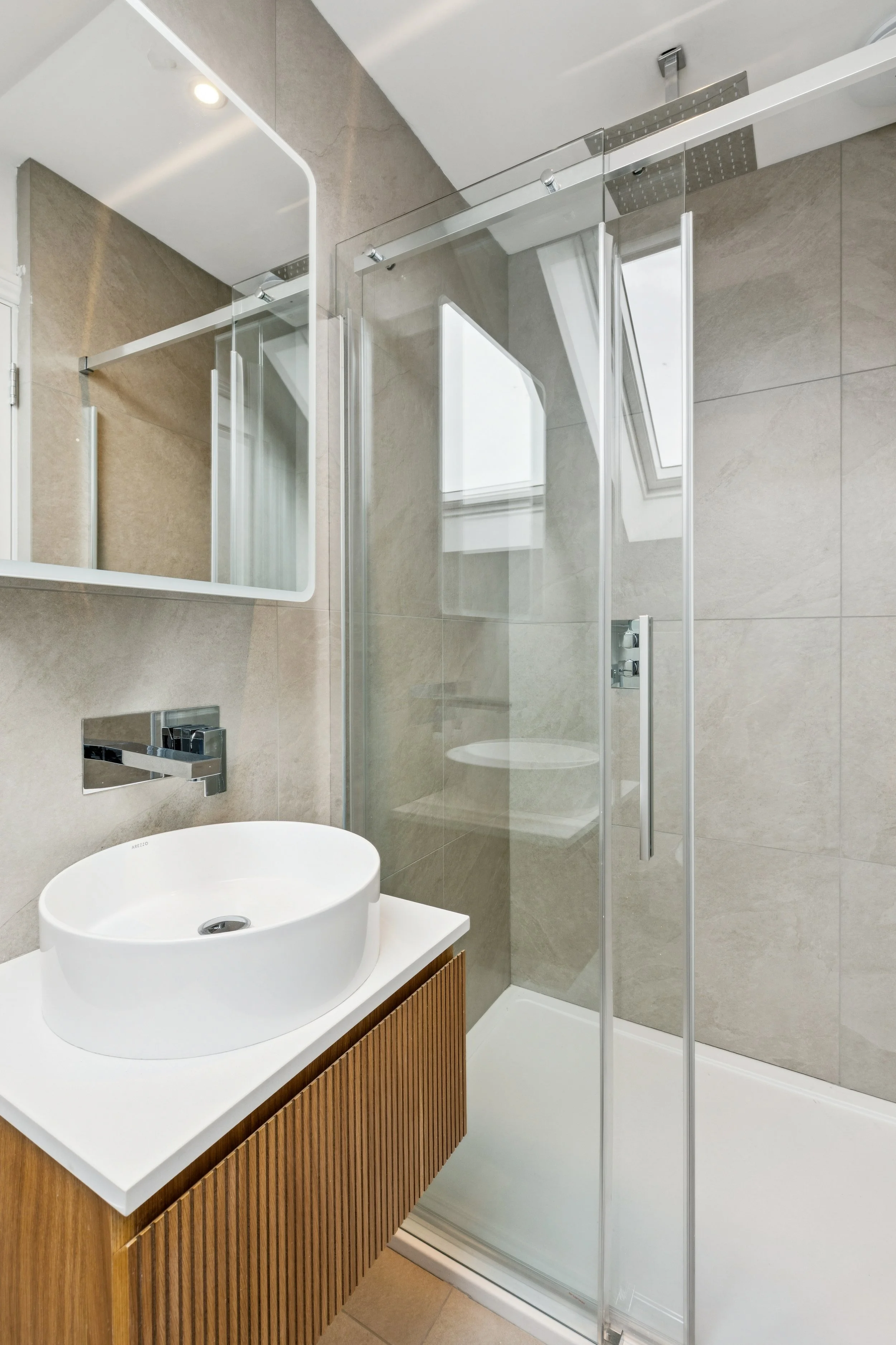 Modern bathroom featuring a vessel sink with a wooden vanity, a glass shower enclosure, and a mirror with built-in lighting.