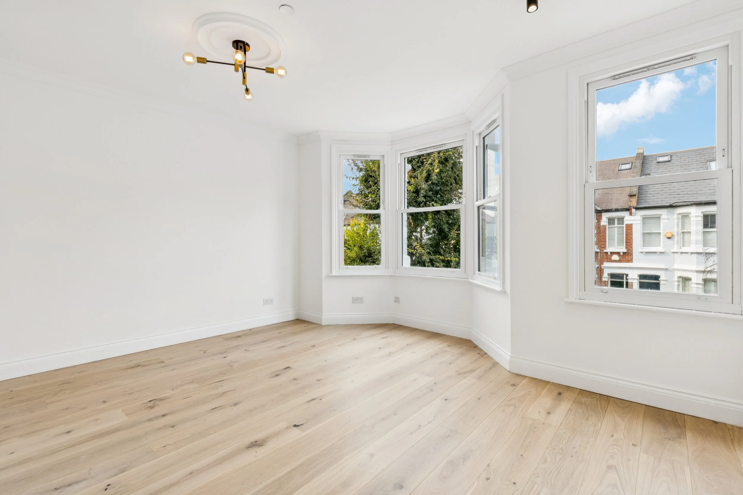 Empty room with white walls, broad windows, and light wooden flooring.