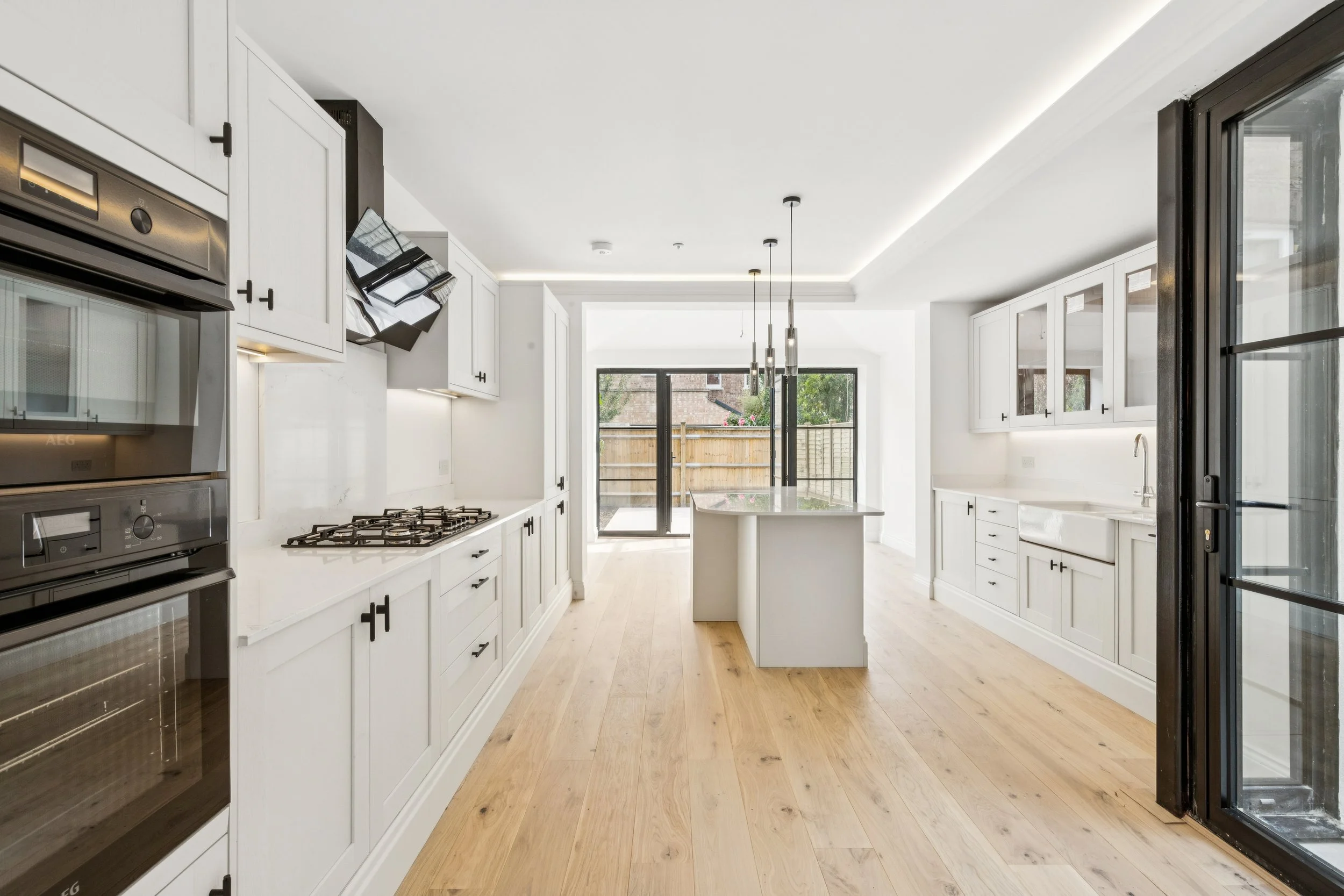 Modern kitchen with white cabinets, wood floors, and large sliding glass doors leading to a backyard.