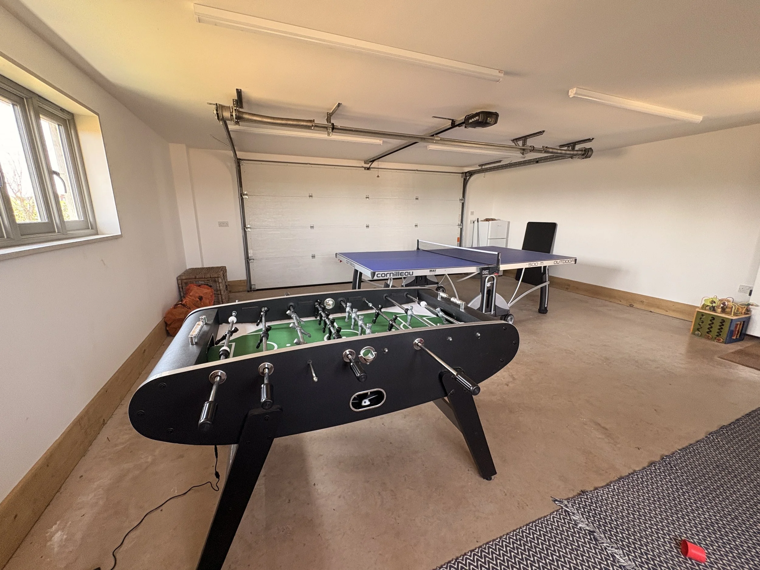 Garage with a foosball table, a ping pong table, and a window on the left wall.