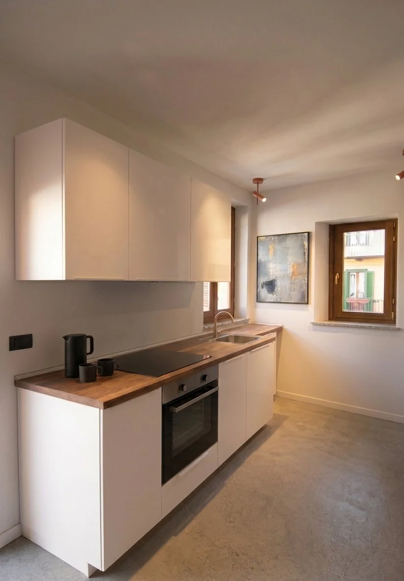 Cucina moderna con counter in legno, armadi bianchi, forno elettrico, piano cottura, due finestre, piastrelle beige e pareti bianche.
