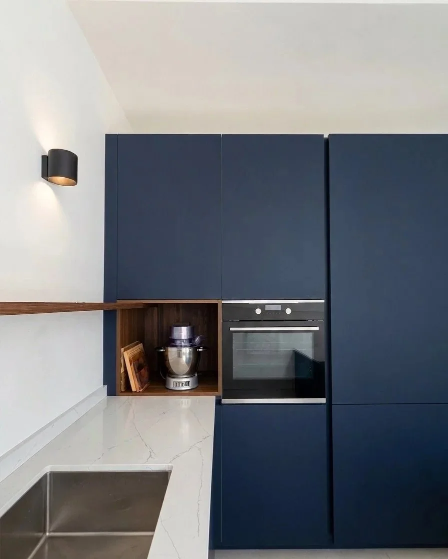 Cucina moderna con armadi blu, forno integrato, piano in marmo bianco, lavello in acciaio e lampada da parete nera