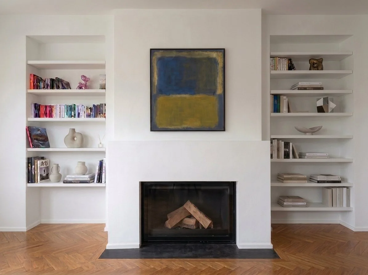 Inserto camino moderno, pareti bianche con mensole, librerie con libri e decorazioni, quadro astratto sopra il camino, pavimento in parquet