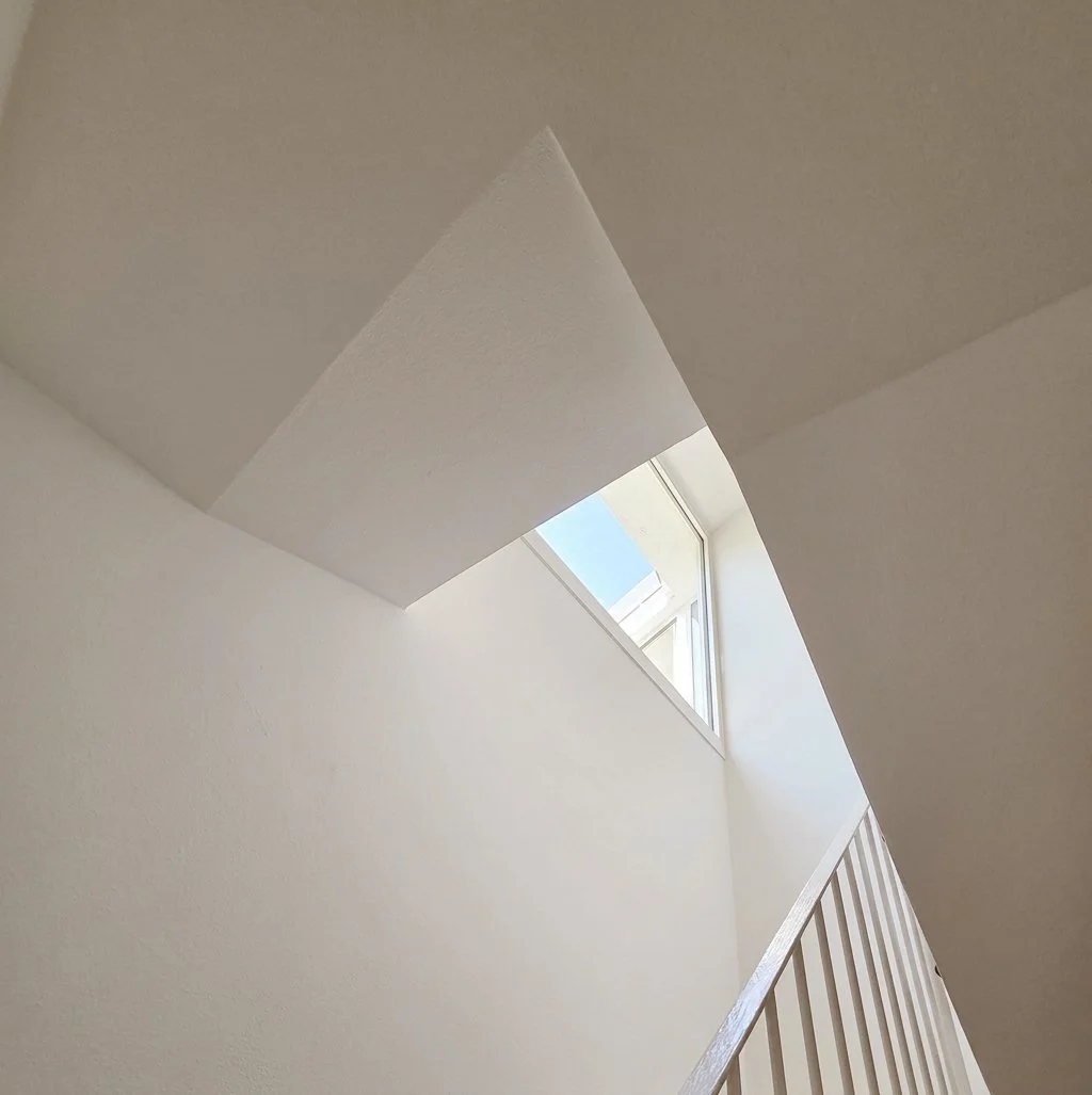 Interno di una casa con pareti bianche, una finestra a soffitto e una ringhiera in legno.