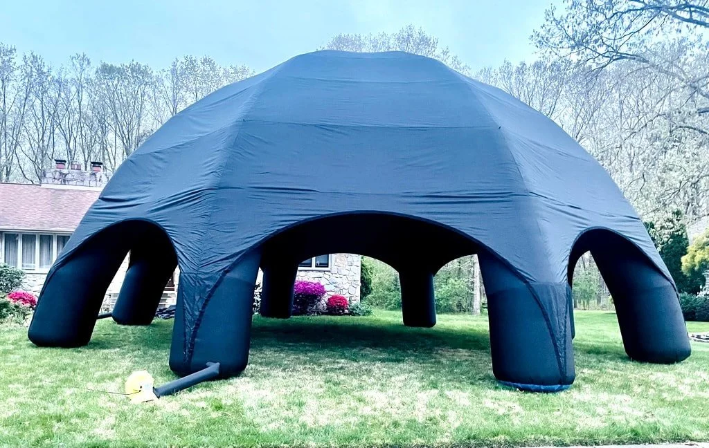 Large black inflatable dome tent set up on a grassy lawn, with a house and trees in the background.