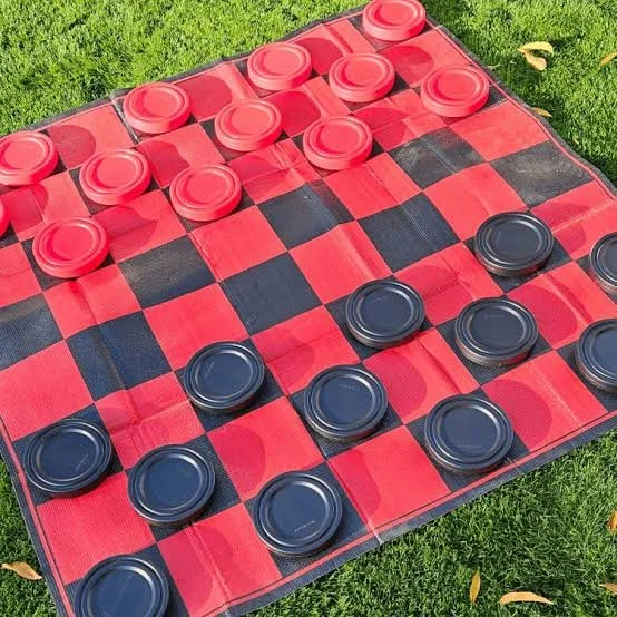 Checkers game on a red and black checkered board outdoors on green grass