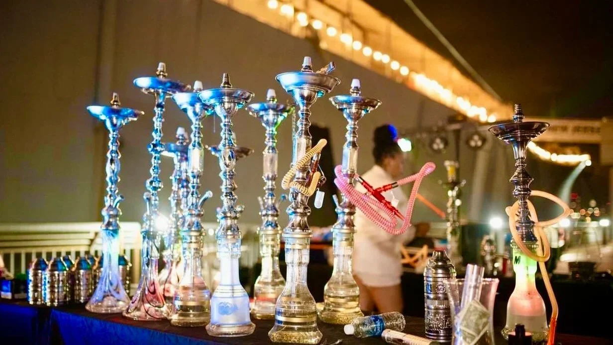 Multiple hookahs on a table with smoking hoses, water bottles, and canisters at a hookah lounge or bar, with an out-of-focus person in the background.