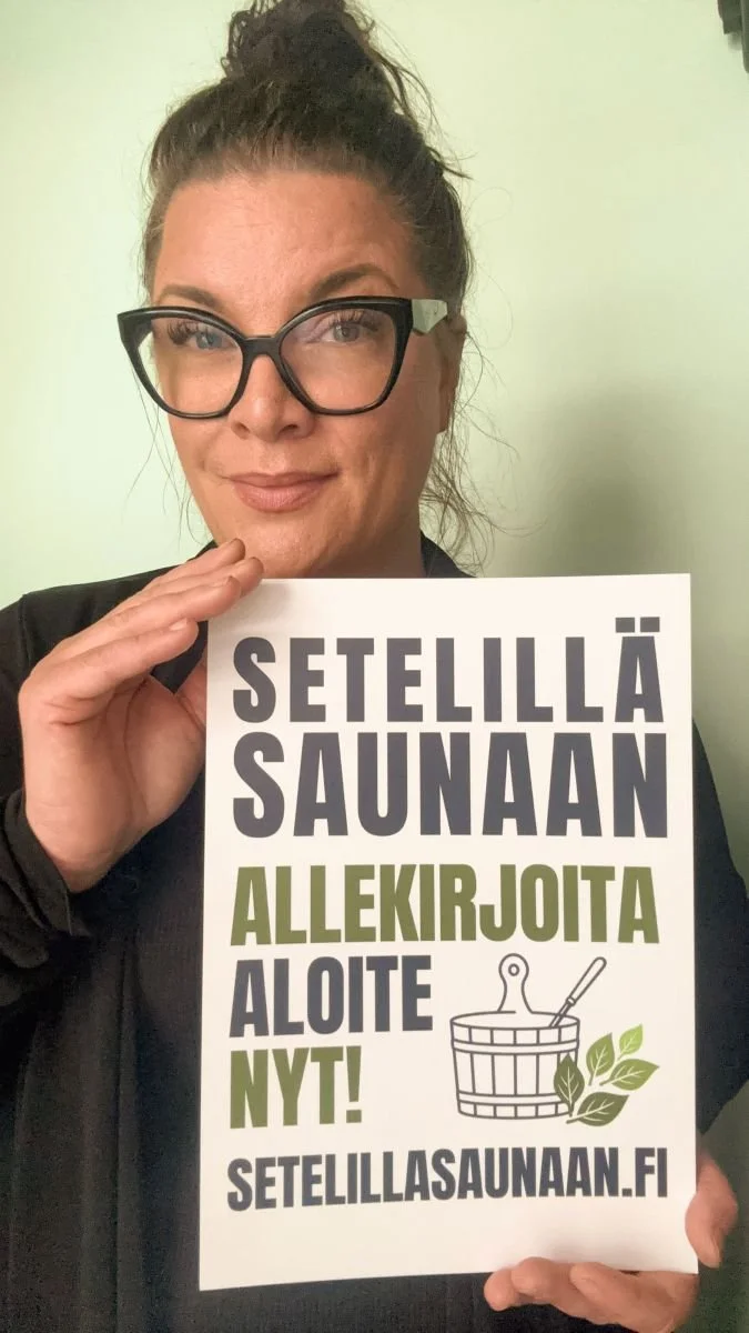 Nainen pitää lapusta, jossa lukee "Setellillä saunaan. Allekirjoita aloite nyt!" otaen osaa saunaverkostojen ja -liikkeiden kampanjaan.