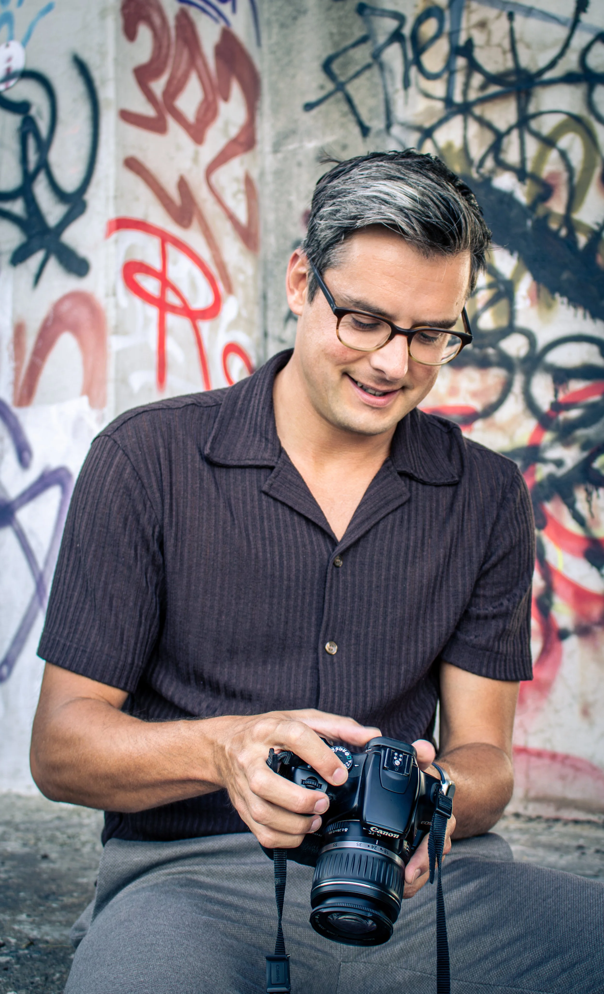 Man zit op de grond voor een graffiti-betaalde muur en bekijkt een digitale camera.