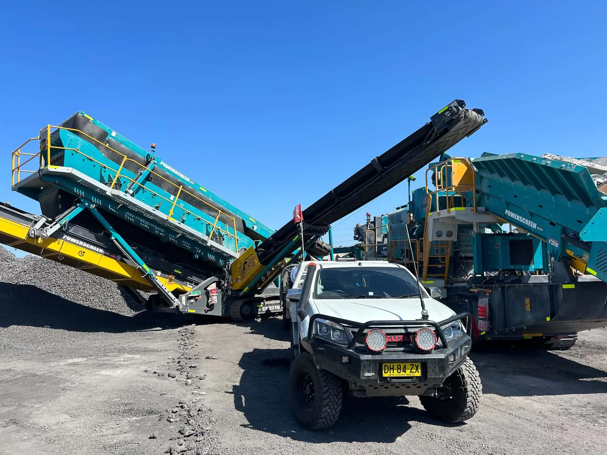 Construction vehicles and equipment on a dirt lot under a clear blue sky