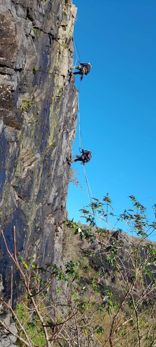 Rope technician descending a steep rock face against a blue sky