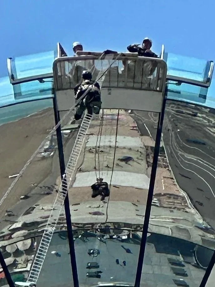 Team members climbing a ladder on a tall structure, viewed from above