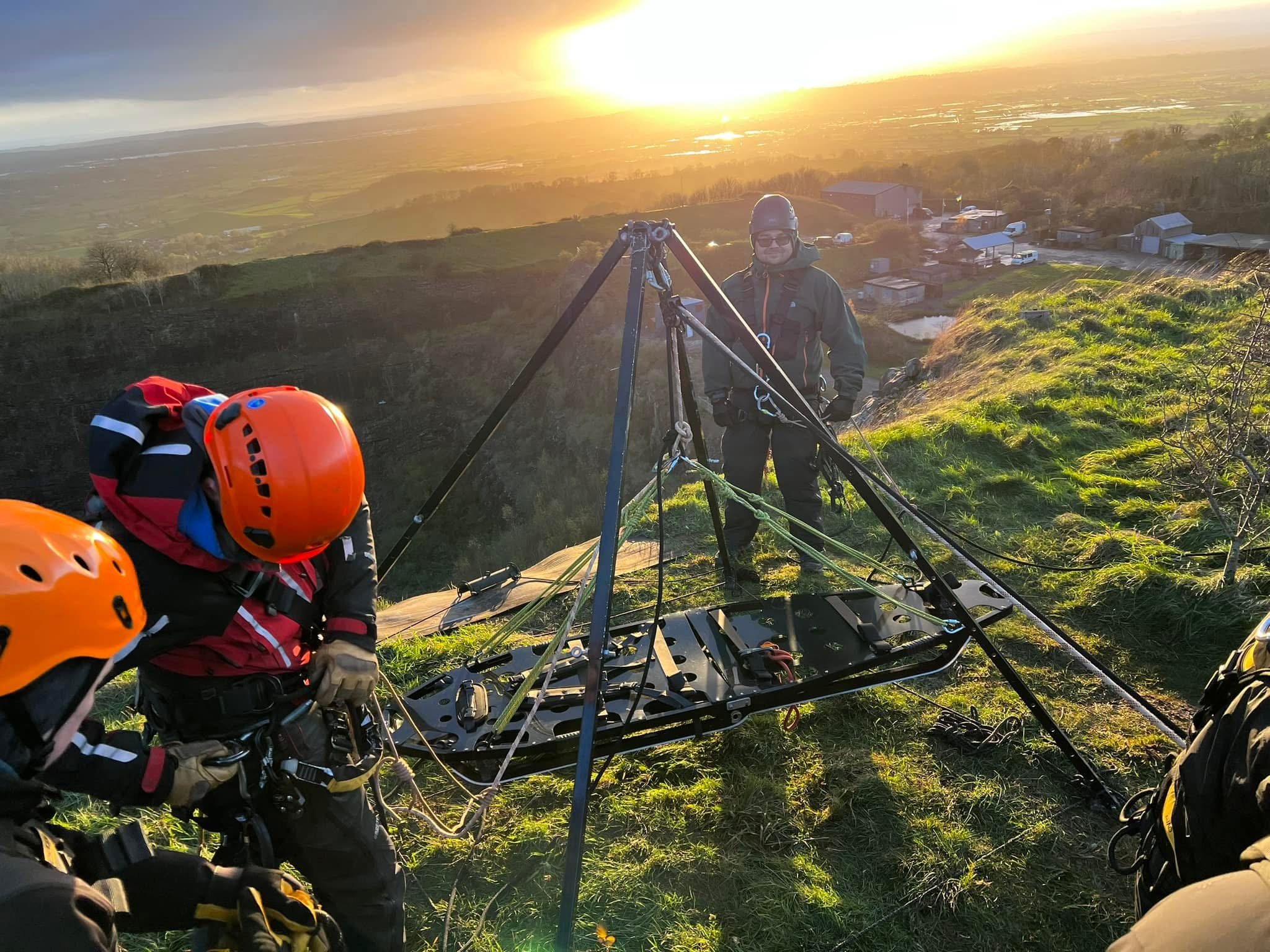 Rope rescue team in helmets rigging a tripod system on a hillside at sunset
