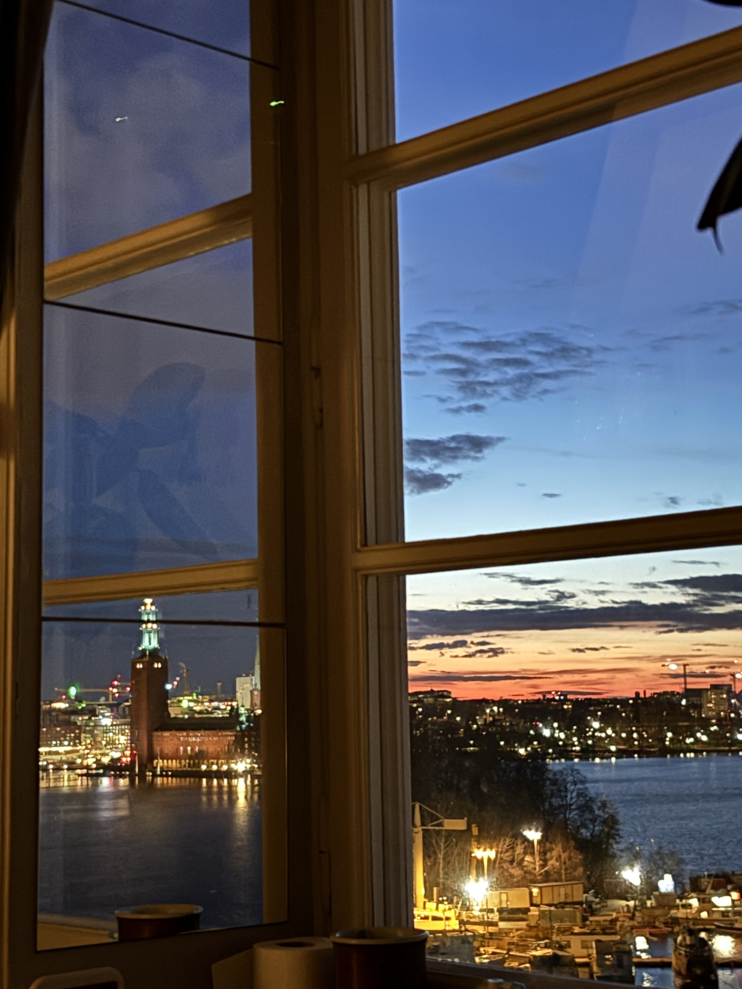 Söder Mälarstrand through an open wooden window with the city hall and a sunset in the background.