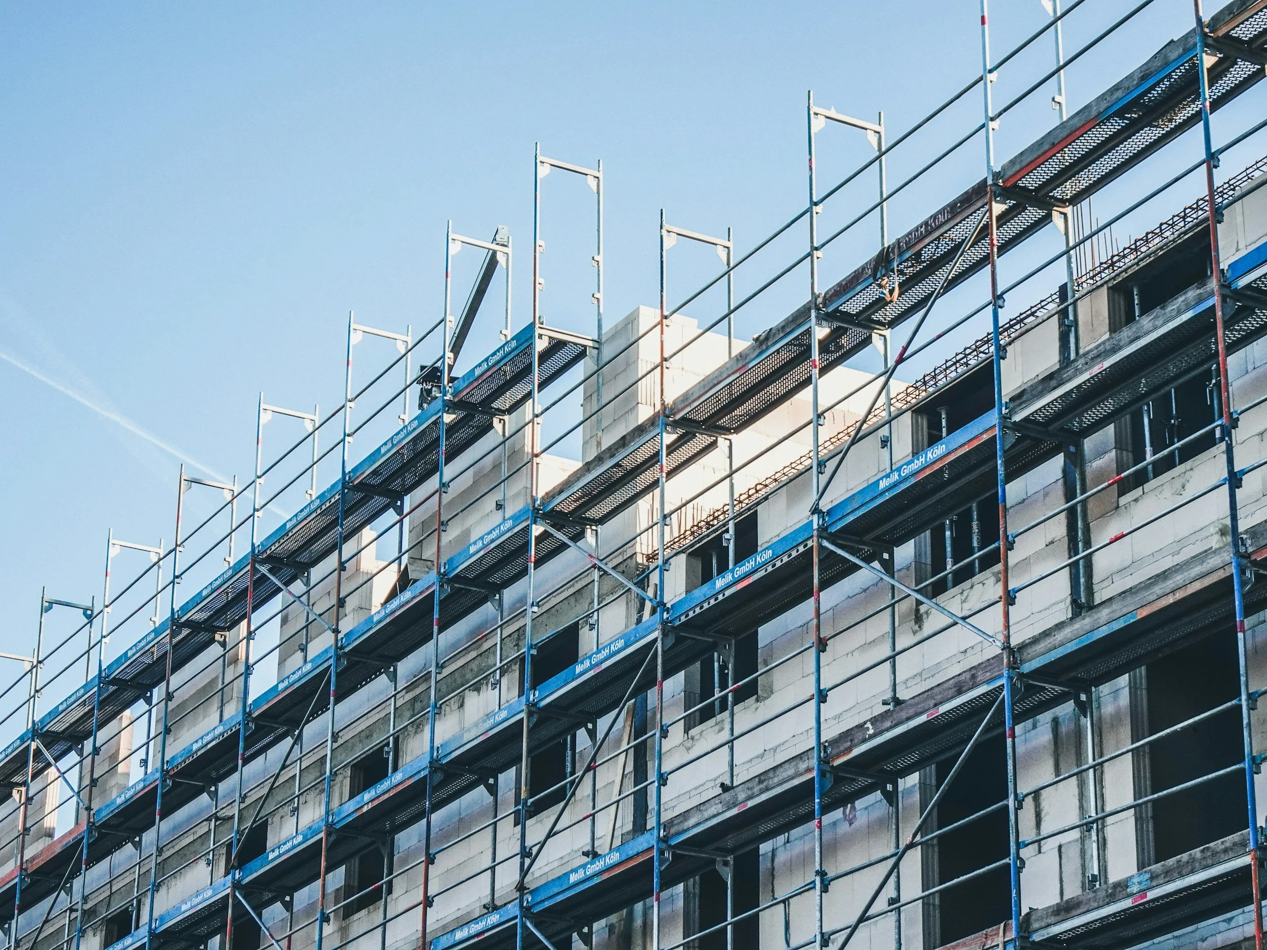 Construction scaffolding set up along the side of a building under construction or renovation against a clear blue sky.