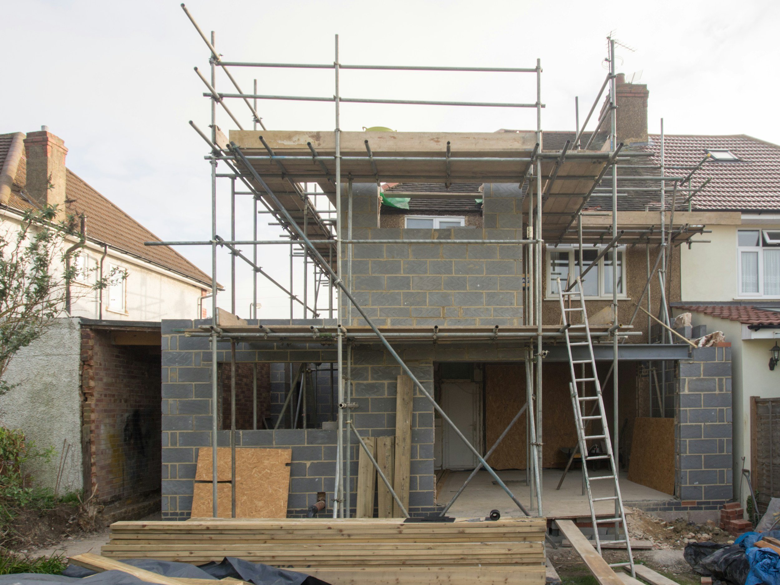 Construction site of a house with scaffolding, brick walls, and building materials in the foreground.