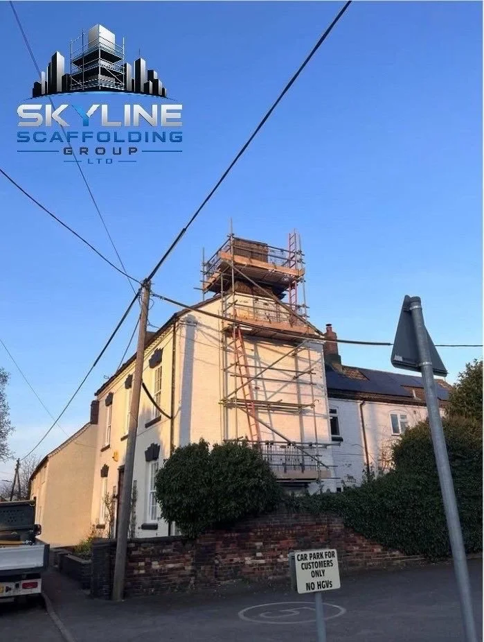 A building under renovation with scaffolding on the front, and a sign indicating parking restrictions. The sky is clear and blue.