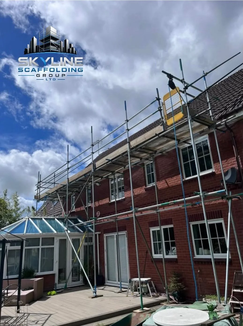 Scaffolding set up around a brick house exterior with a partially enclosed porch, under a partly cloudy sky, with a logo for Skyline Scaffolding Group in the top left corner.