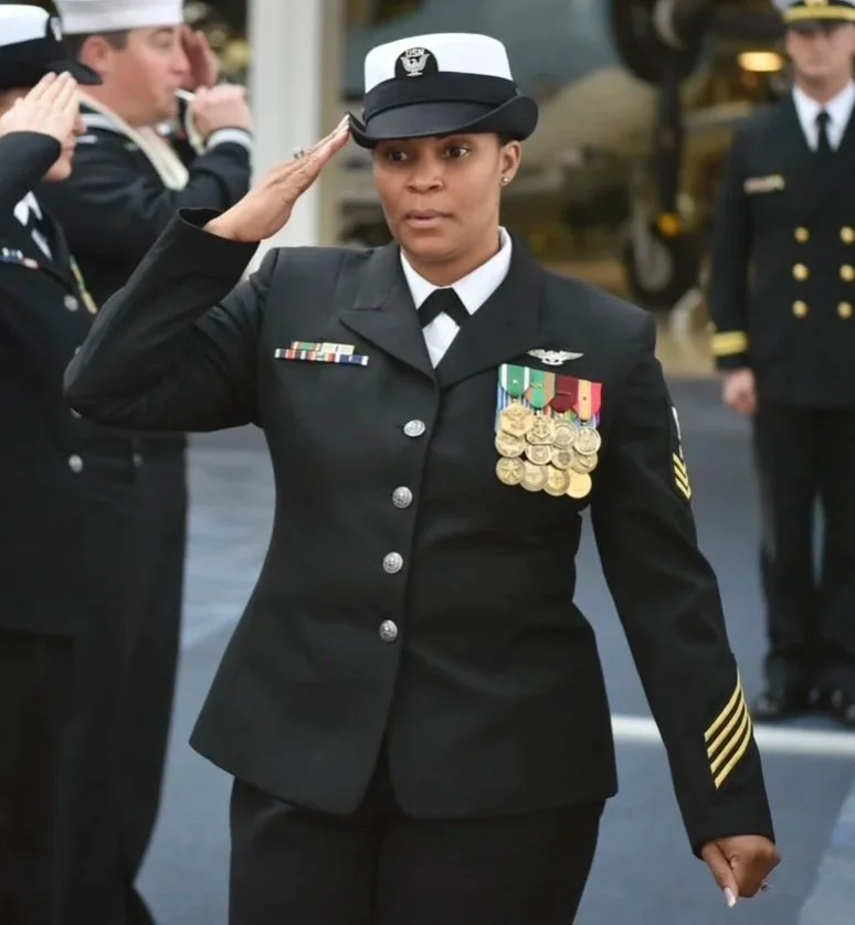 Decorated female U.S. Navy officer saluting in dress uniform outside a building