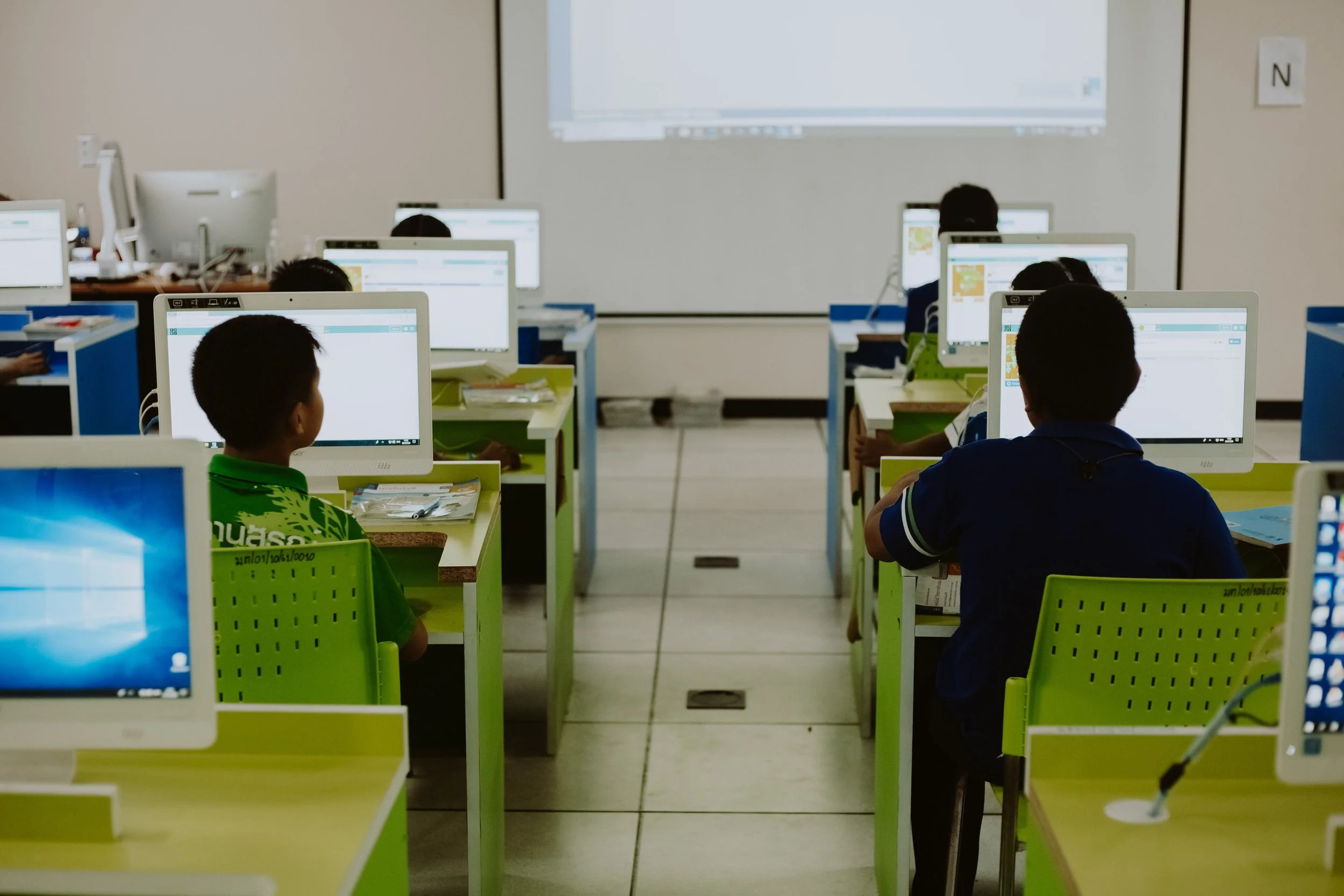 A classroom with students working on computers, facing a whiteboard or projection screen at the front of the room. Kamtron's work with Government.