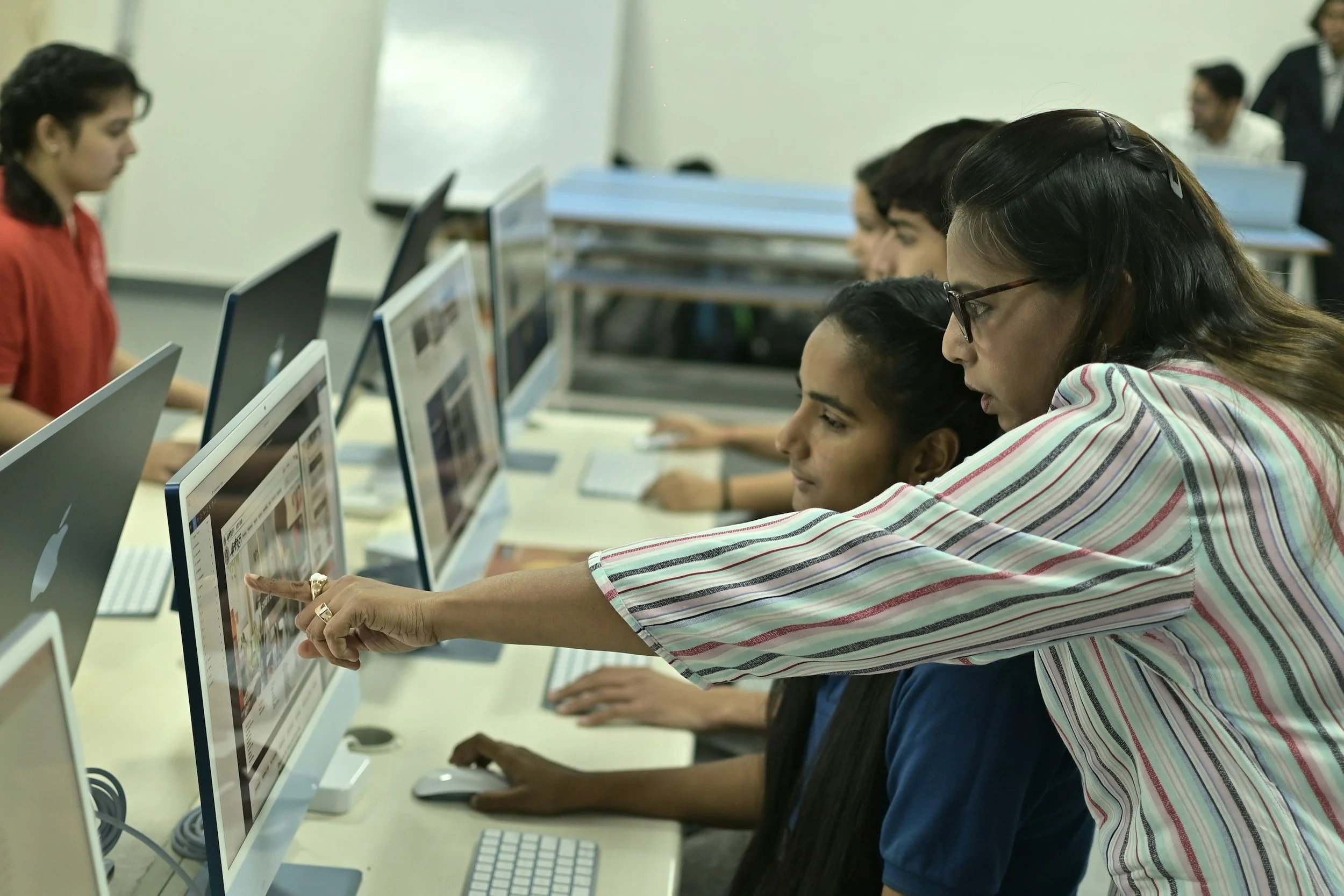 A woman in a striped shirt assisting a student with a computer in a classroom setting. Kamtron's work in the education industry.