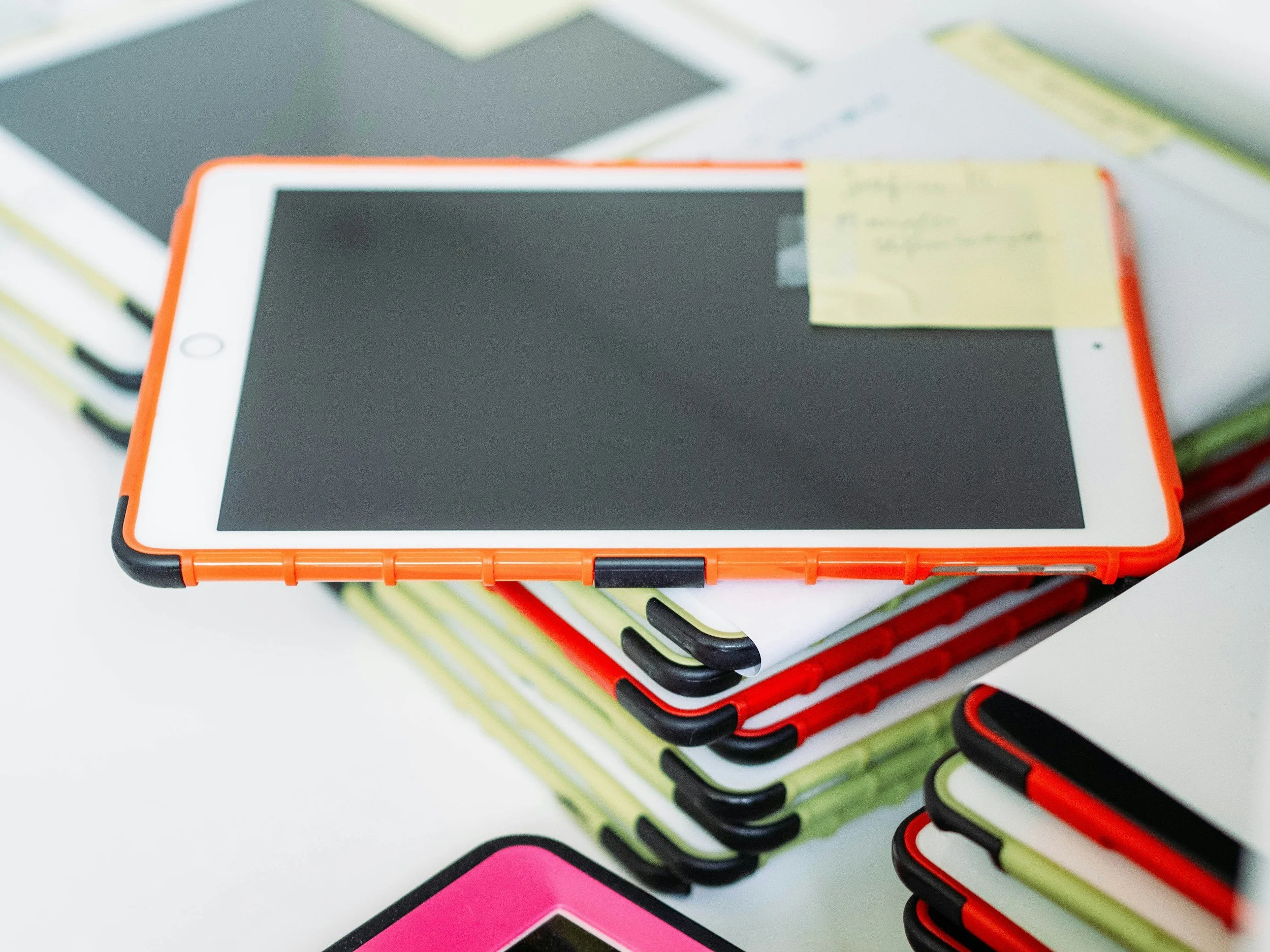 Stack of tablets with colorful covers and a post it sticker on top. Kamtron Systems deals in tablets and chromebooks.