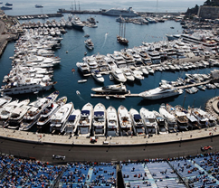 View of a marina filled with yachts and boats, with a curved dock and a large outdoor seating area in the foreground.